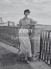 A black and white picture portraing a woman standing near the sea, with a shirt and a silky skirt. | Seventy Venezia